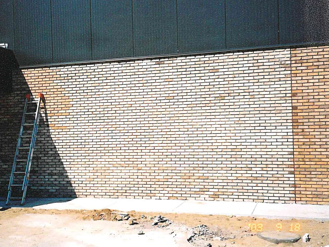 A long stretch of showroom brick in 2003 with a ladder leaning against it, the wall running from pale cream in the sun to a warmer tan at the right
