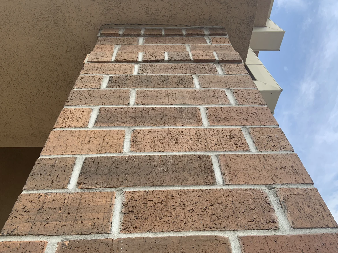 A brick column photographed from its base looking up to the soffit, the units running in mixed browns and tans against the sky