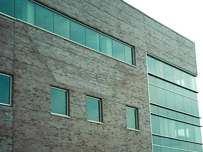 The elevation in 1999, its gray brick blotched with pale and darker areas beside a full-height glazed bay