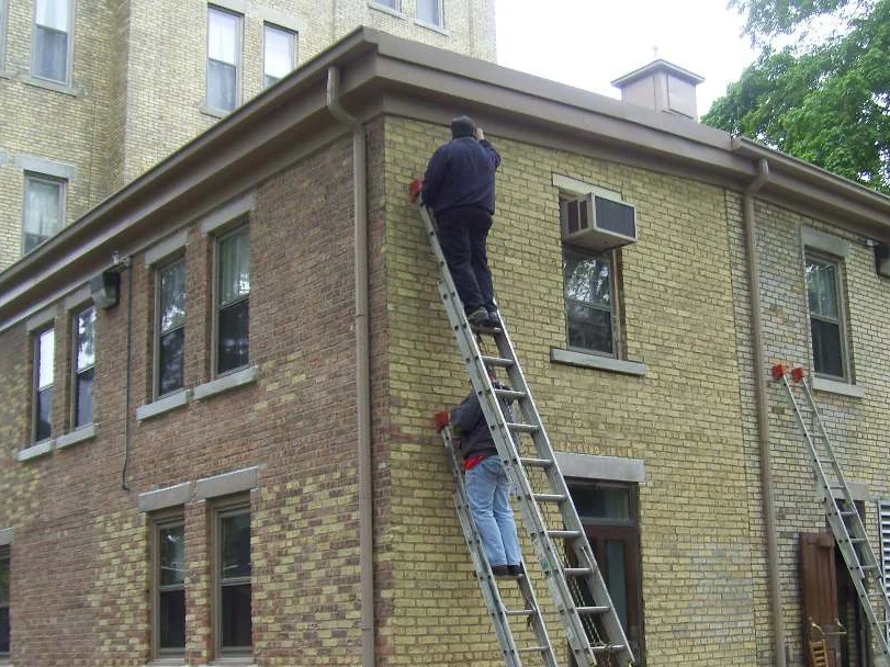 The outside corner during the 2006 work, the near return wall still red brown while the long elevation beyond it already carries the buff range, two men on extension ladders at the corner