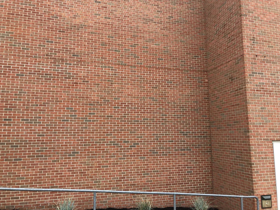 An inside corner where two brick walls meet in 2019, the courses running unbroken around it in one red and brown range above a planted bed