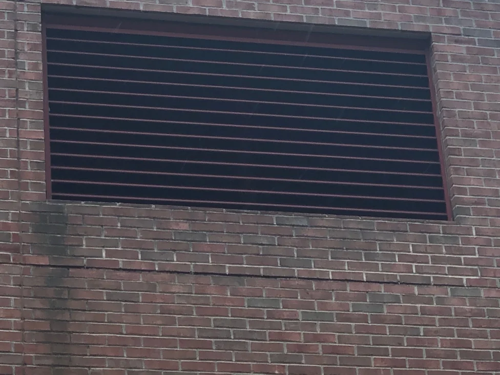 Close view of a louvred vent set into the brick in 2019, the units around it in a mixed red, brown and grey range with pale mortar joints