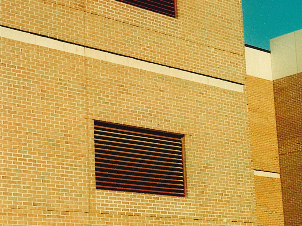 A tall wall in 2001 with two louvred vents stacked one above the other and cast stone banding between them, its brick reading pale buff against the red brick wing standing behind it on the right