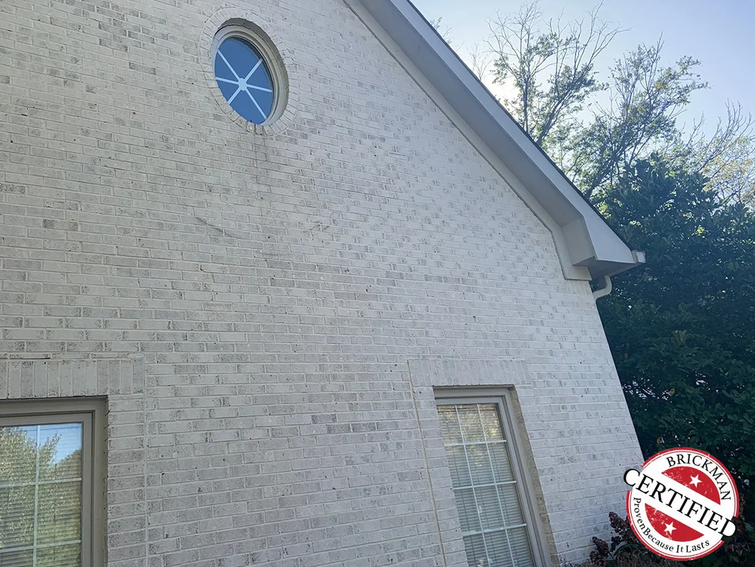 The same gable end and its two tall windows in 2019, the blended brick carrying the Brickman certification stamp at the lower right