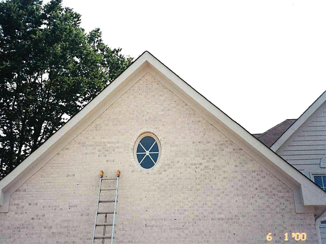 The whole gable end of the house with a ladder leaning against it, the brick a pale cream broken by scattered bare white units