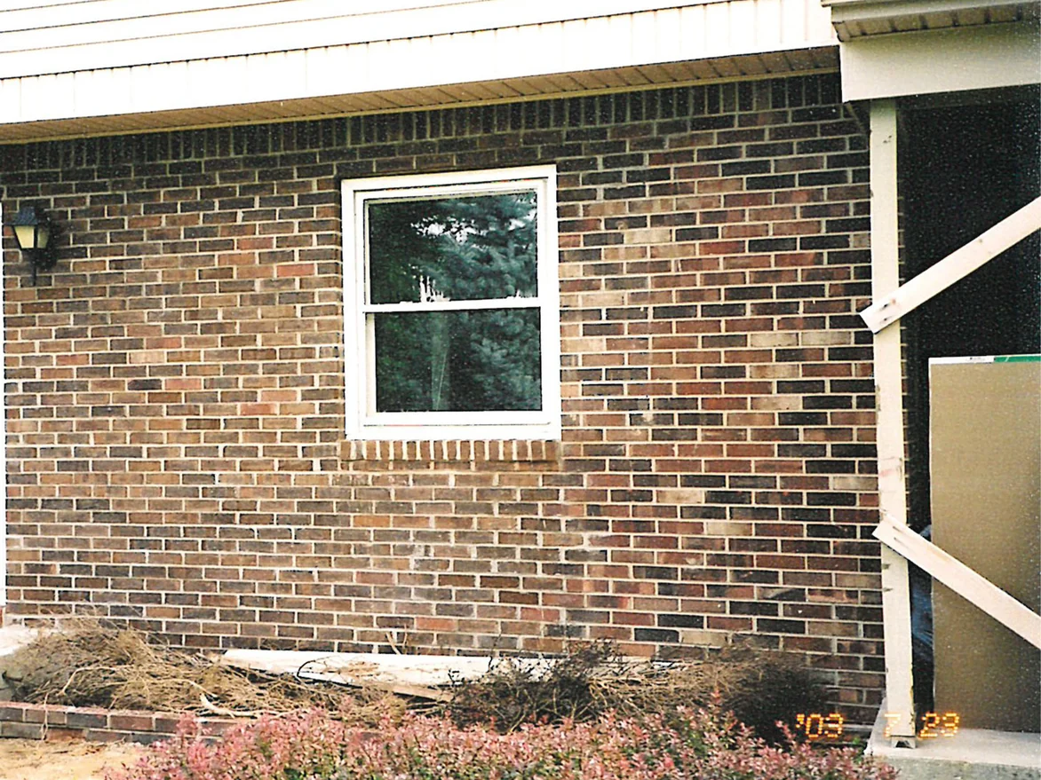 The wall beside the front door in 2003, a single window in a field of red and dark brown brick with the beds dug out below it