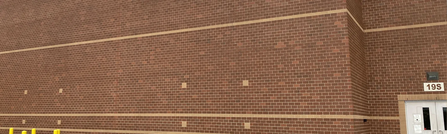 The long windowless side wall of the Indianapolis school in 2021, red brown brick at one range with two buff accent courses running its full length