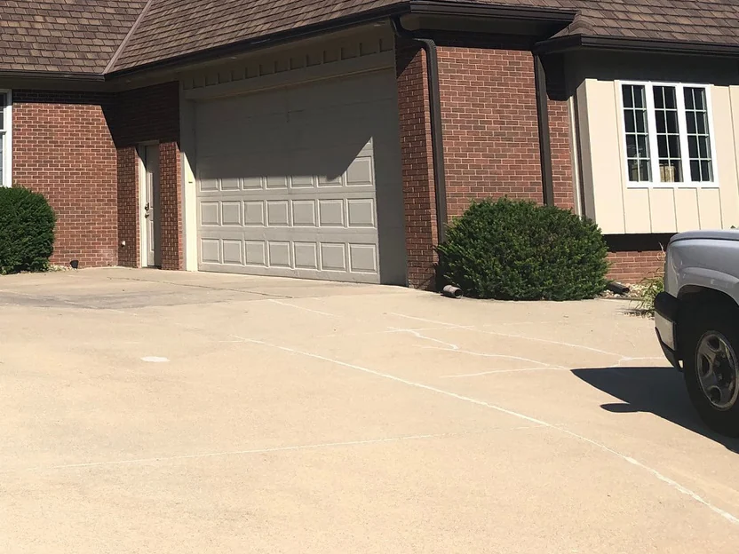 The garage wing in 2019, a tan garage door between two red brick piers with a side door on the left and a board-and-batten bay on the right