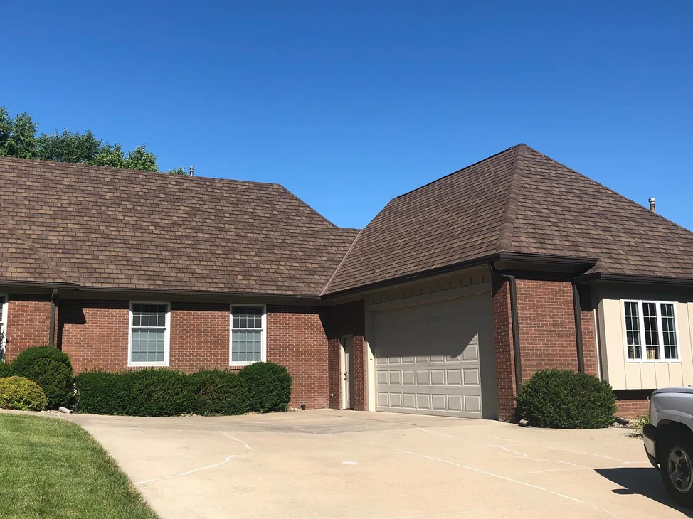 The front of the single-story house in 2019 from the driveway, the main wall on the left and the garage wing on the right in the same red brick under a brown shingle roof