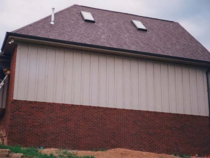 The side wall of the addition in 1997 after staining, red brick below tan siding under a hipped roof with two skylights, a ladder against the corner