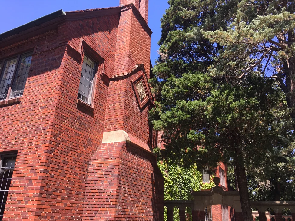 The chimney breast running up the corner of the house in 2019, a carved panel set into the brick above a stone offset.