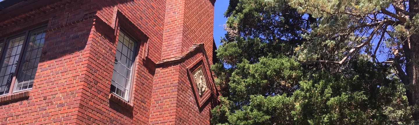 The chimney breast rising up the corner of the house in 2019, a carved panel set into red brick