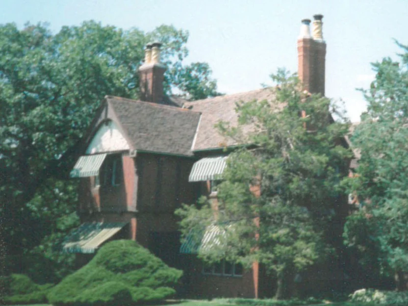 The house seen from the lawn behind mature trees, two chimney stacks standing above a steep roof
