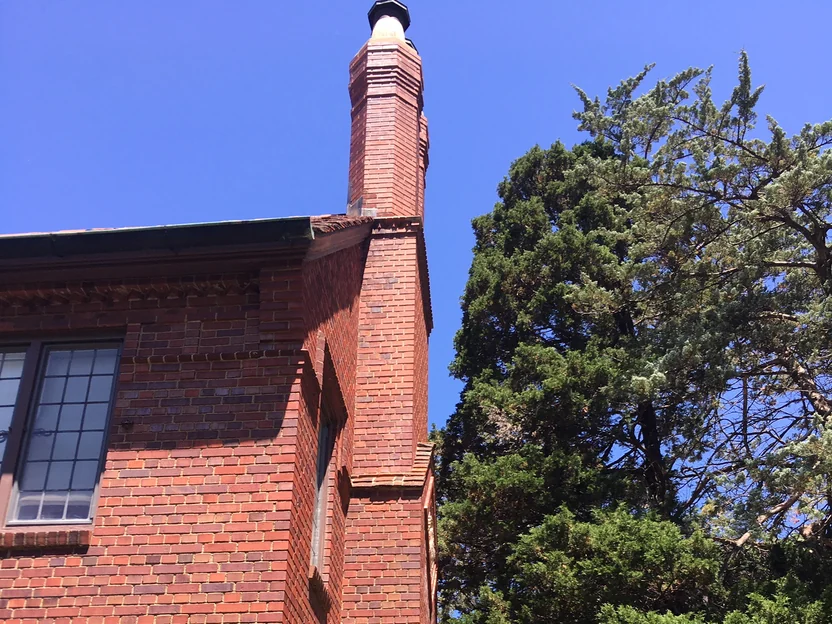 The chimney stack standing clear of the tiled roof in 2019, its brick the same red as the wall it rises from