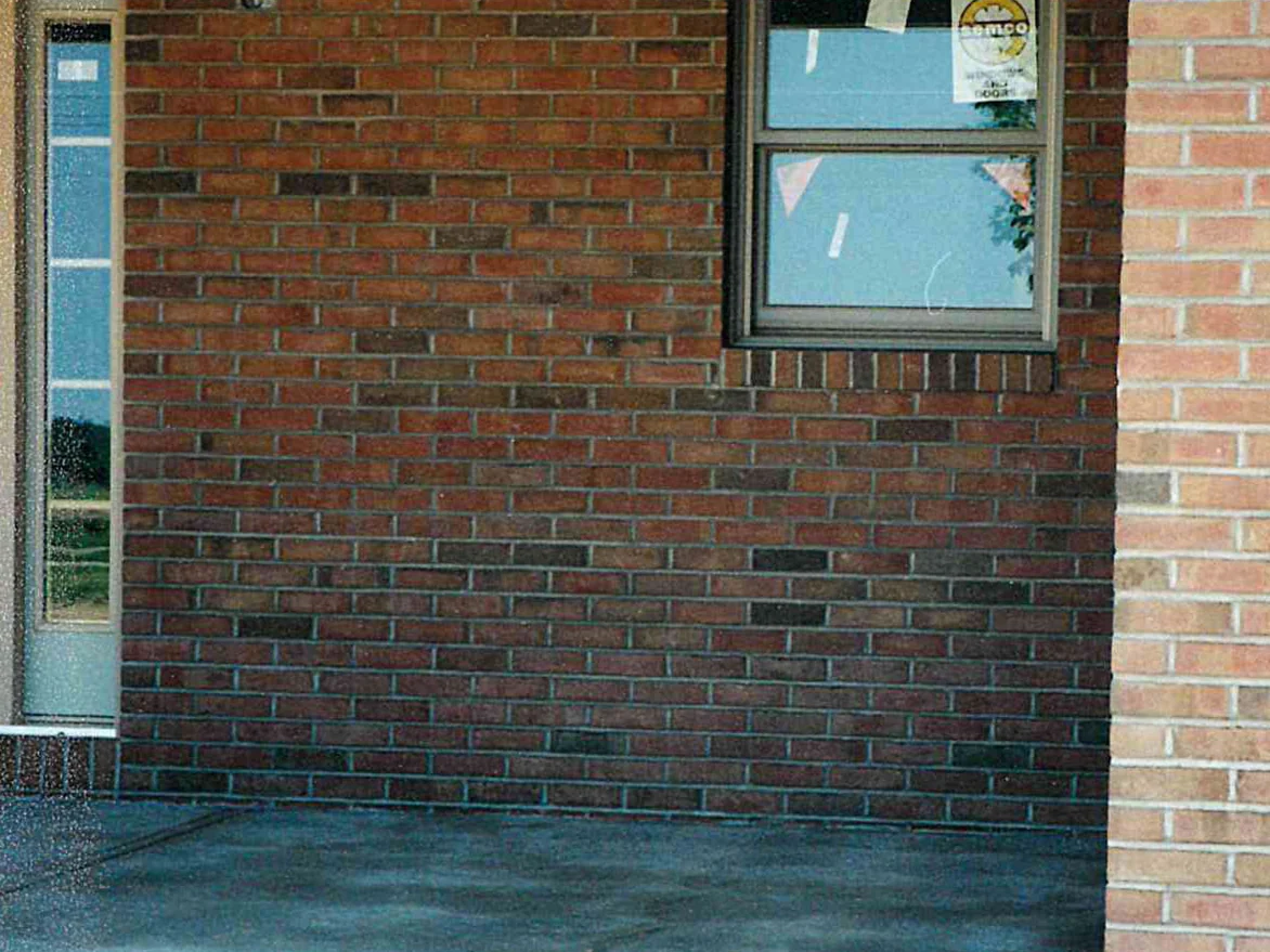 The wall beside the front door after staining in 1999, a sash window with a manufacturer's sticker still on the glass and the brick reading as one darker red range