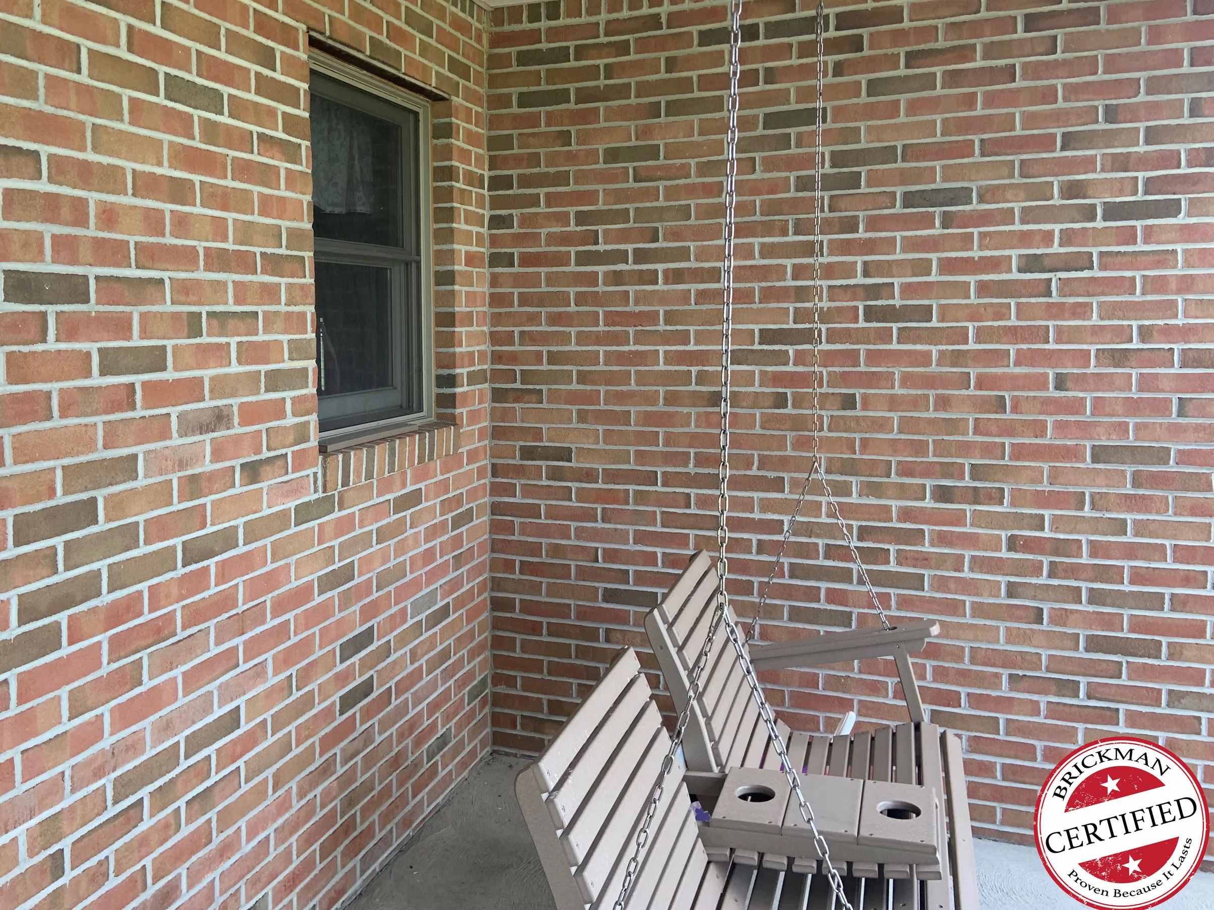 The same inside corner of the porch in 2019, a swing hanging in front of two brick walls that now read as one continuous red and tan range