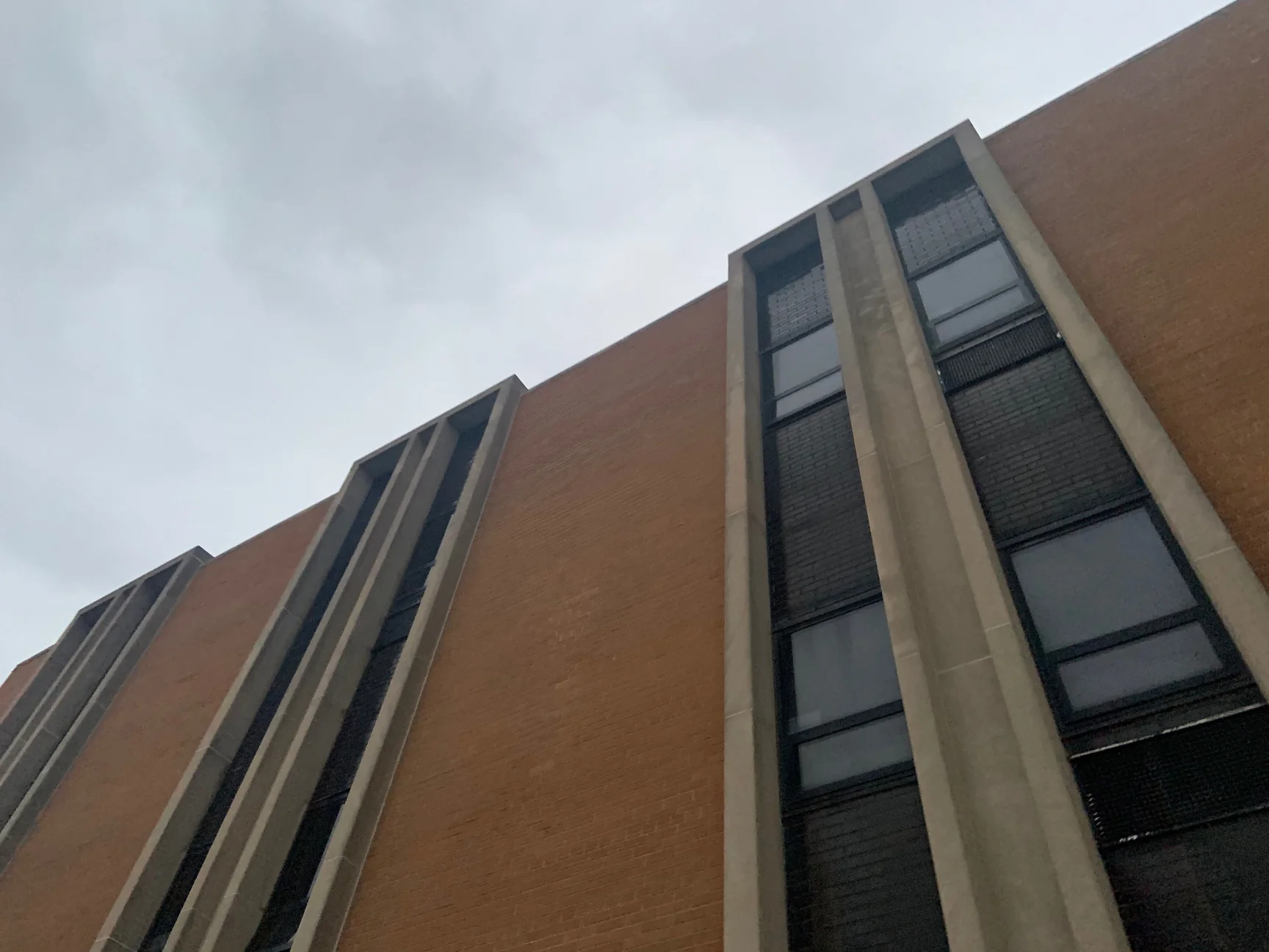 The upper facade in 2019, three bays of concrete window fins stepping along an even brown brick wall