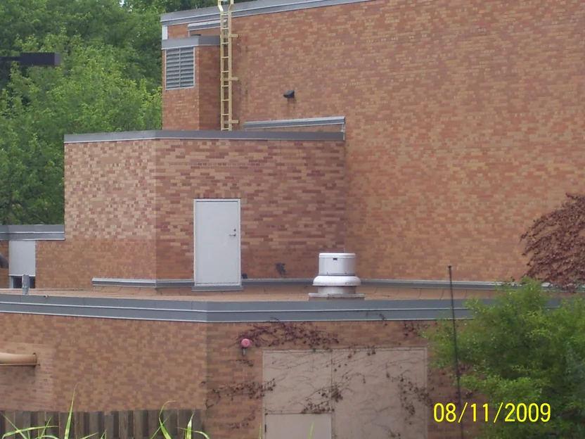 The stepped upper stories of the building in 2009, tan and orange blended brick over a flat roof with a service door, a roof ladder and a vent