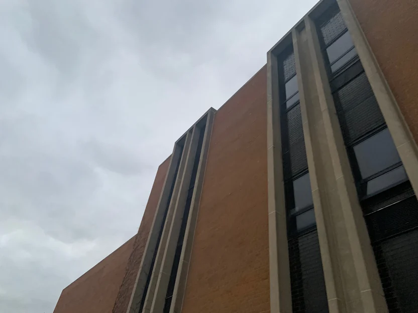 Looking up at the building in 2019, tall concrete-framed window slots set into a plain brown brick wall under a grey sky