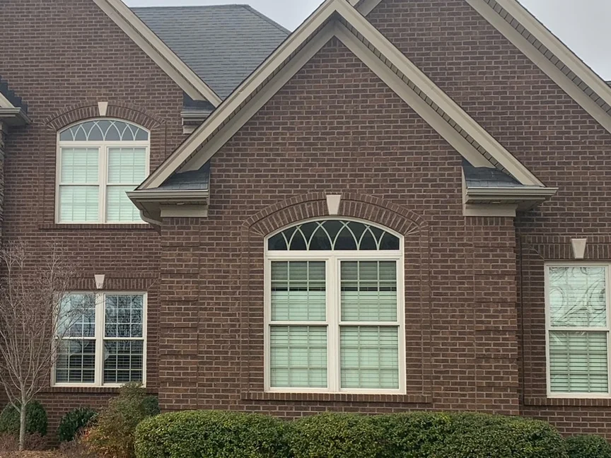 The same gable elevation in 2019, the mortar still dark against the brick around the arched window, with grown shrubs along the foundation