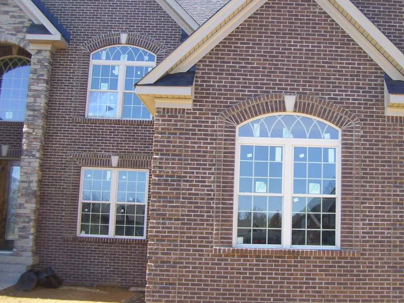 The gable elevation in 2010, pale mortar joints standing out against dark brown brick around a tall arched window, with bare dirt at the foundation