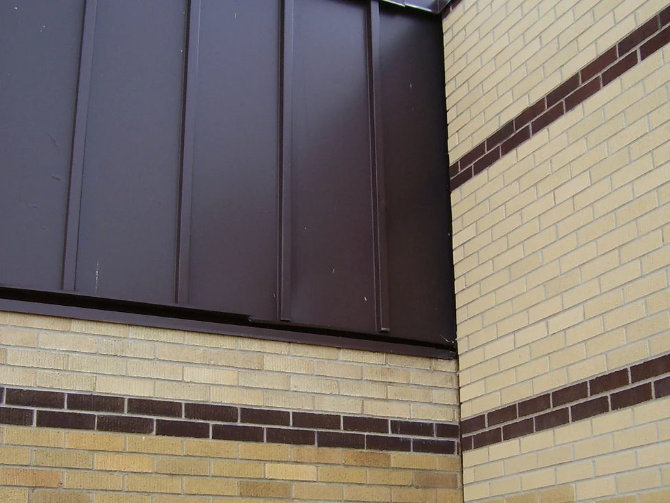 An inside corner where two walls meet, the wall on the left in mottled yellow and tan brick and the wall on the right in a paler cream, both banded with dark brown courses