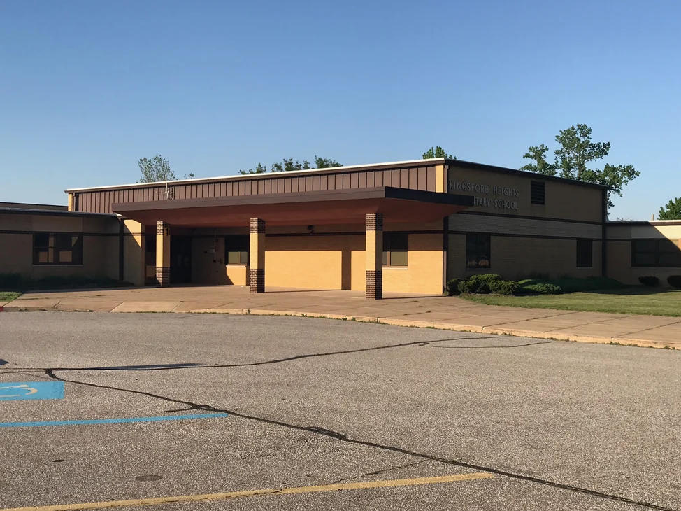 The whole front of the school from the car park in 2019, its buff brick running one tone across every bay.