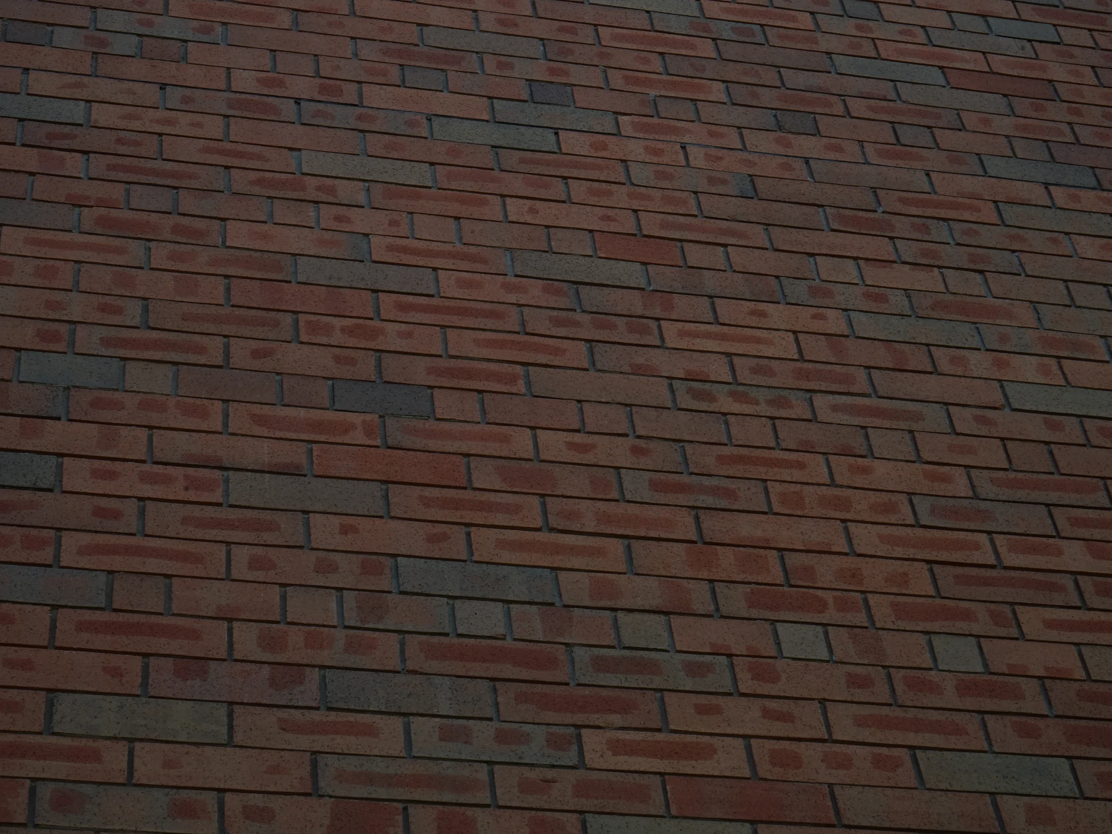 Close view of the stained brick in 2019, the units running from orange through deep red to near-black against grey mortar joints