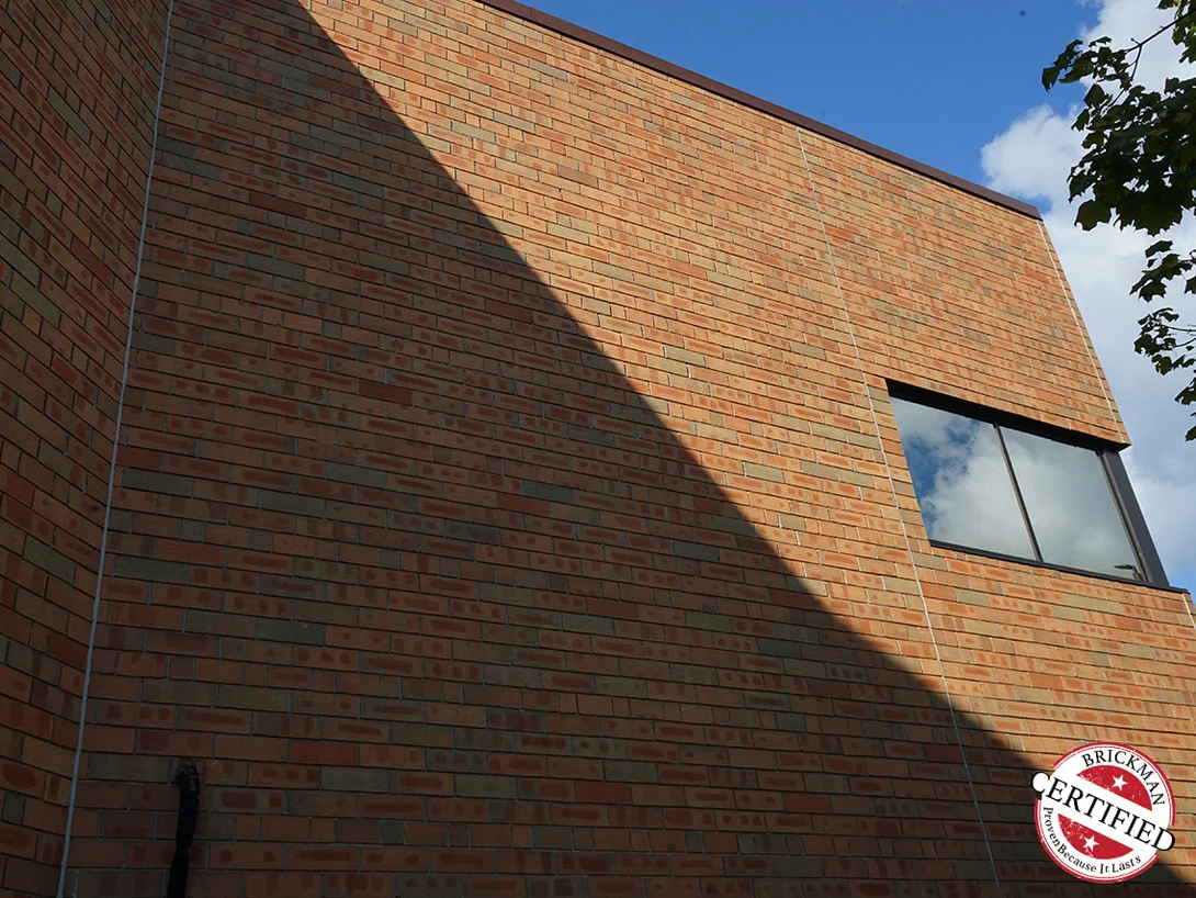 A blank brick elevation of the office in 2019 with a shadow line running diagonally across it and the certification stamp at the lower corner