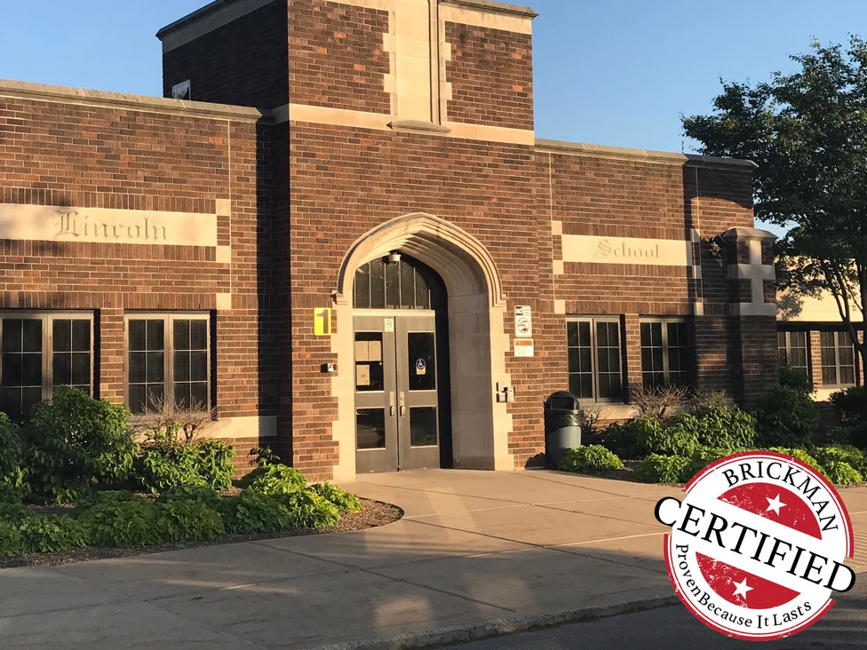 The school entrance in 2019 with the Brickman certified stamp across the corner of the frame, the brick an even blend of browns and reds