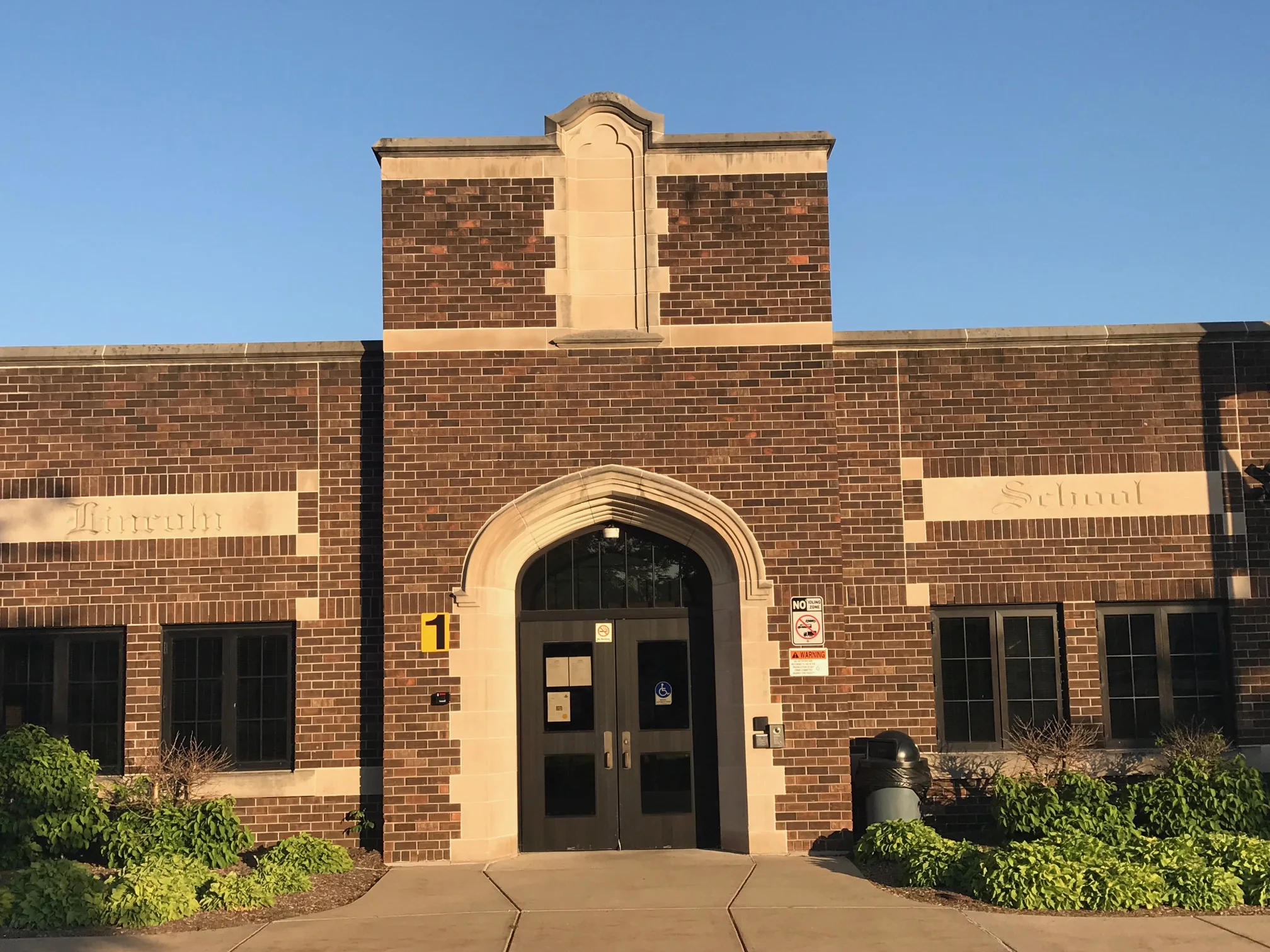 Close view of the school's entrance bay in 2019, the individual brick units reading dark brown and red with scattered lighter ones among them