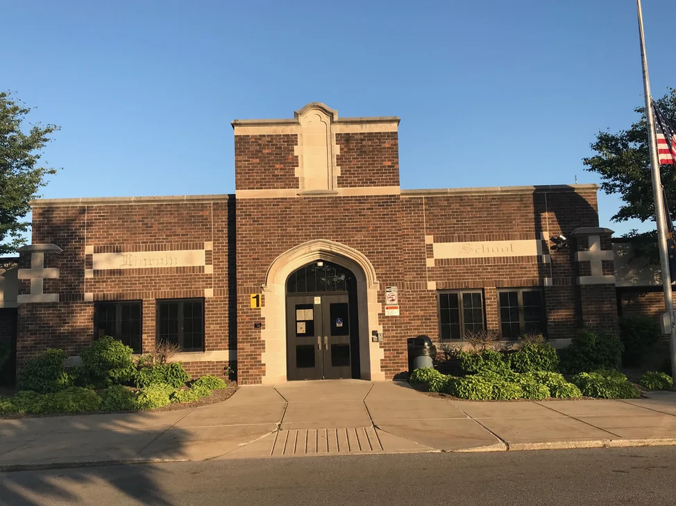 A brick school with a canopied entrance, its brickwork one even range