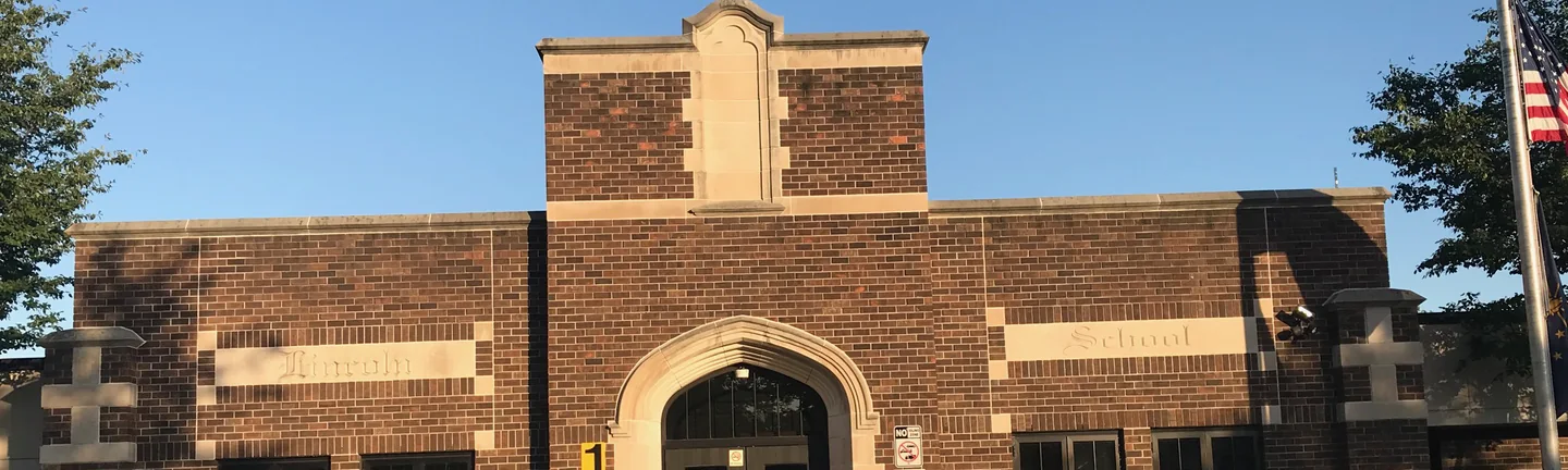The front wall of a school in 2019, brick running between two carved stone bands