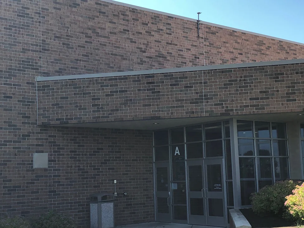 The corner where the school's tall block meets the lower entrance wing in 2019, the brick running in mixed browns and greys across a vertical joint