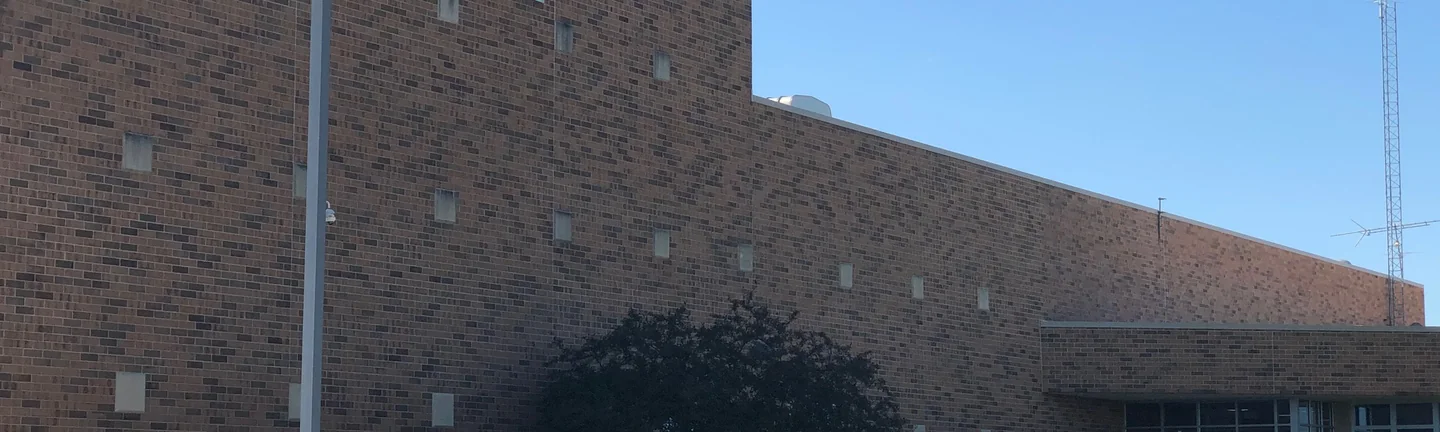 The long brick front of a high school in 2019, the wall reading as one range from end to end