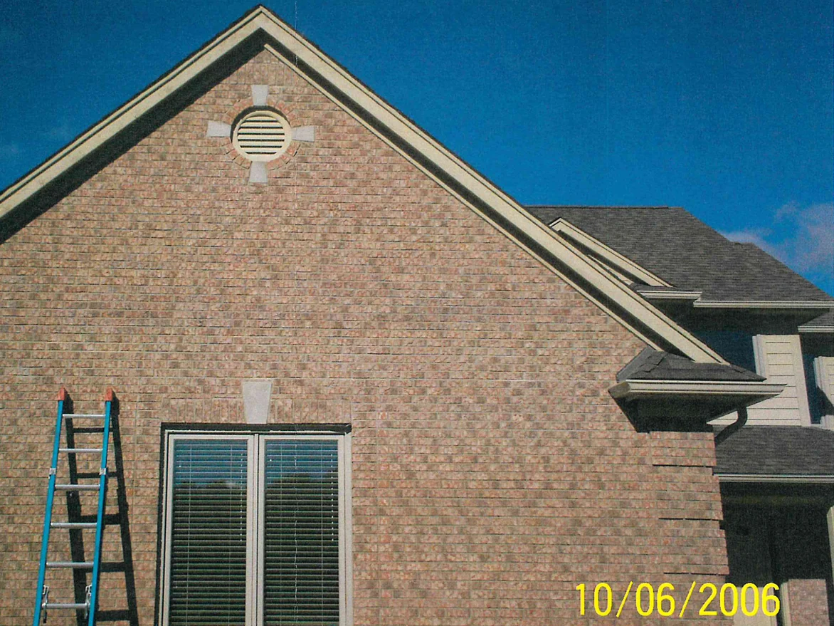 The same gable end on 6 October 2006 after the light brick was darkened, an extension ladder leaning against the wall beside the window under a clear sky