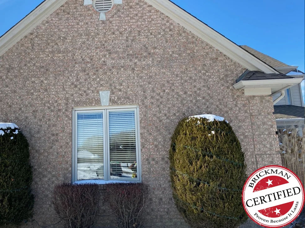 The gable end of the Leonard house in 2021 with snow on the shrubs in front of it, the blended brick reading as one range from the window up to the vent in the peak, with the certification stamp in the corner