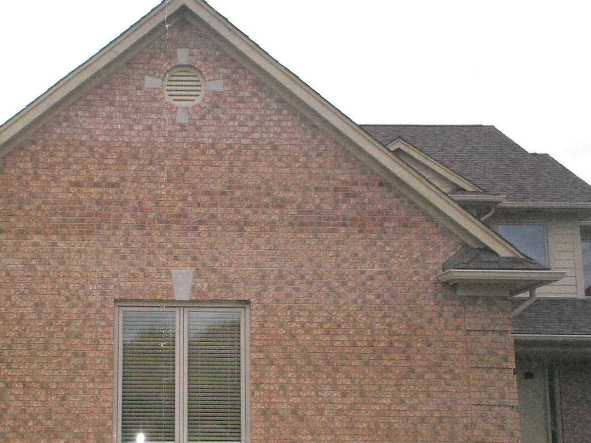 The gable end of the house on 5 October 2006 before staining, red and tan blended brick under a cream fascia with a round louvered vent in the peak and one window below it