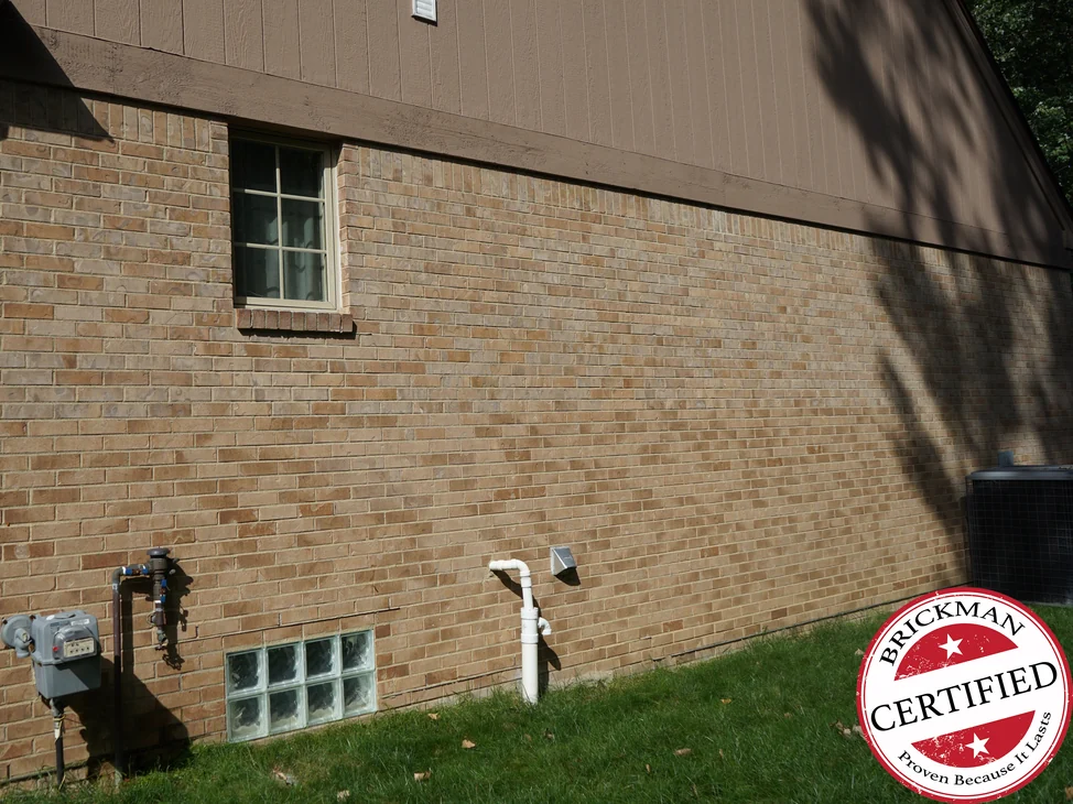 The long side wall of the house in 2019, its brick carrying one even tan and cream range from the corner to the far end, with the Brickman certified stamp in the corner of the frame.