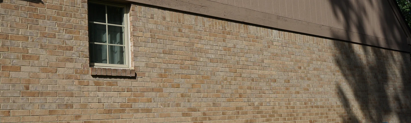 The side wall of the house in 2019, its brick reading as one even tan range beneath brown board and batten gable siding