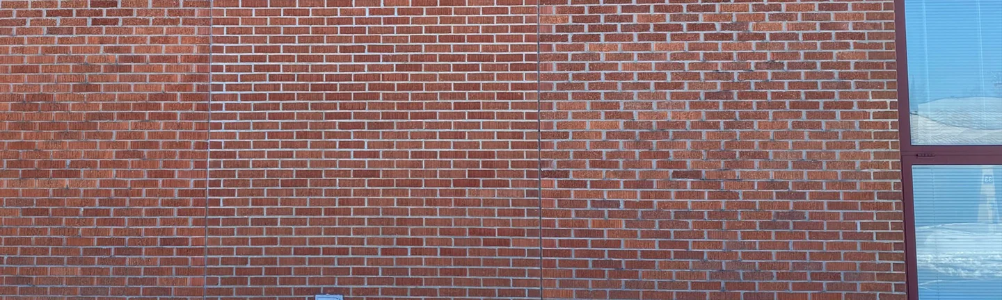 The red brick wall of the high school in 2021 under its blue corrugated metal cladding, the filled-in panel reading as one range with the brick beside it