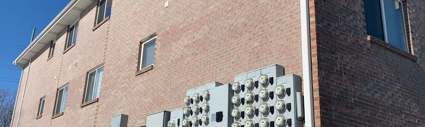 The long side wall of the Lincoln apartment building in 2021, pink brown brick in direct sun above a bank of electric meters