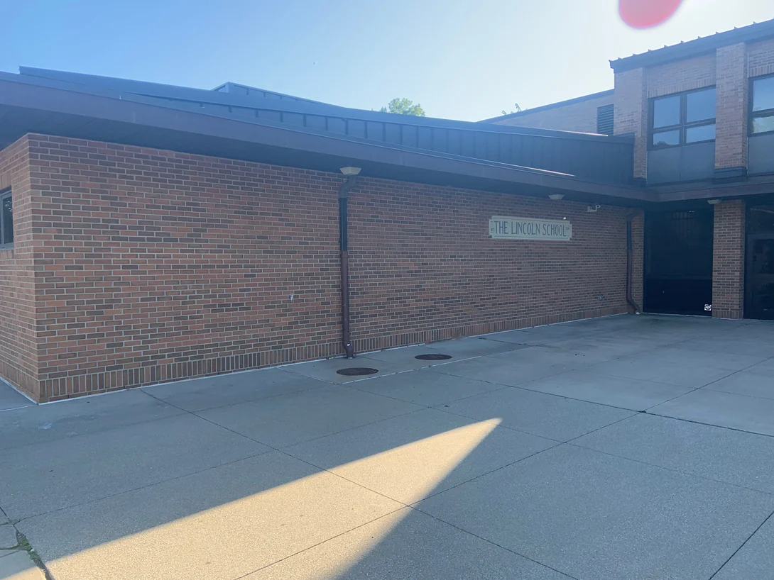 The covered entrance courtyard in 2019, a carved stone panel reading The Lincoln School set into blended red and brown brick