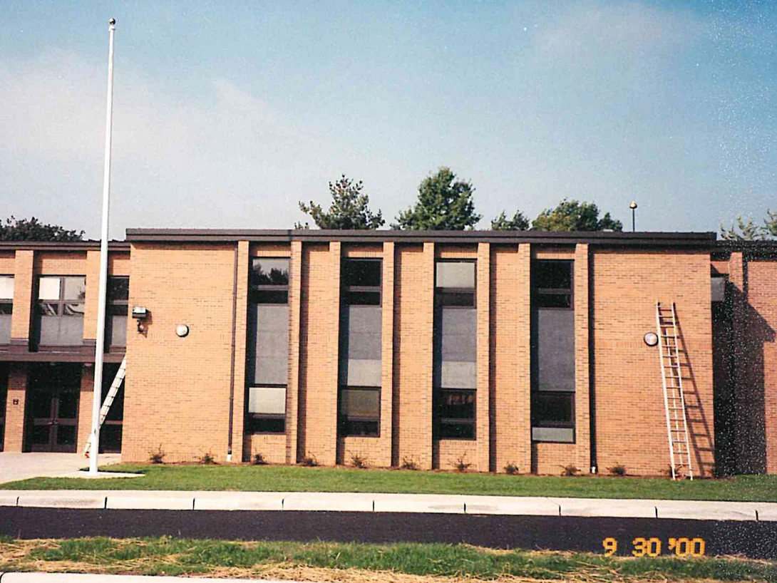 The two-story front of the school in 2000 with a flagpole and a ladder set against the wall, the brick a single uniform tan