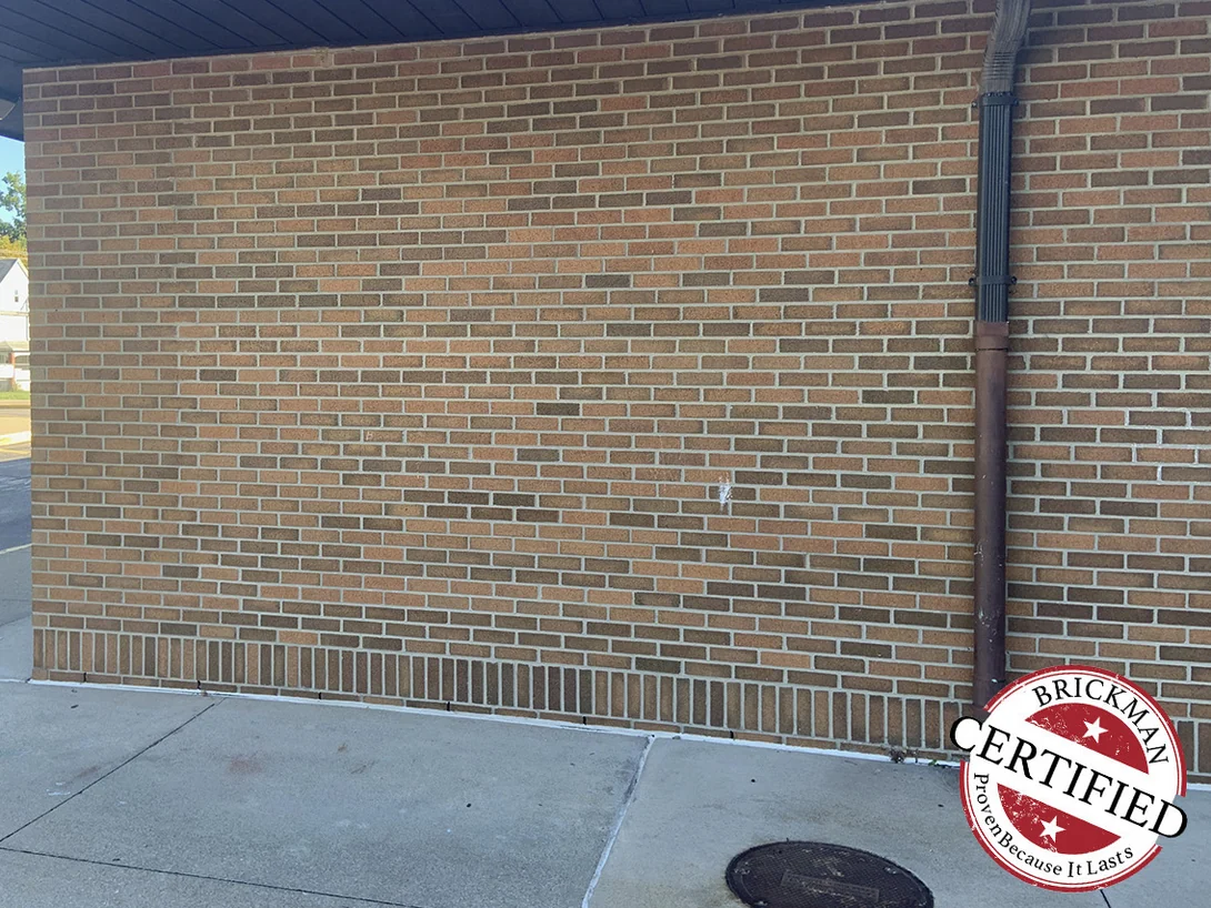 A wall under the entrance canopy in 2019, its brick a mixed range of red, tan and dark brown units with pale mortar joints