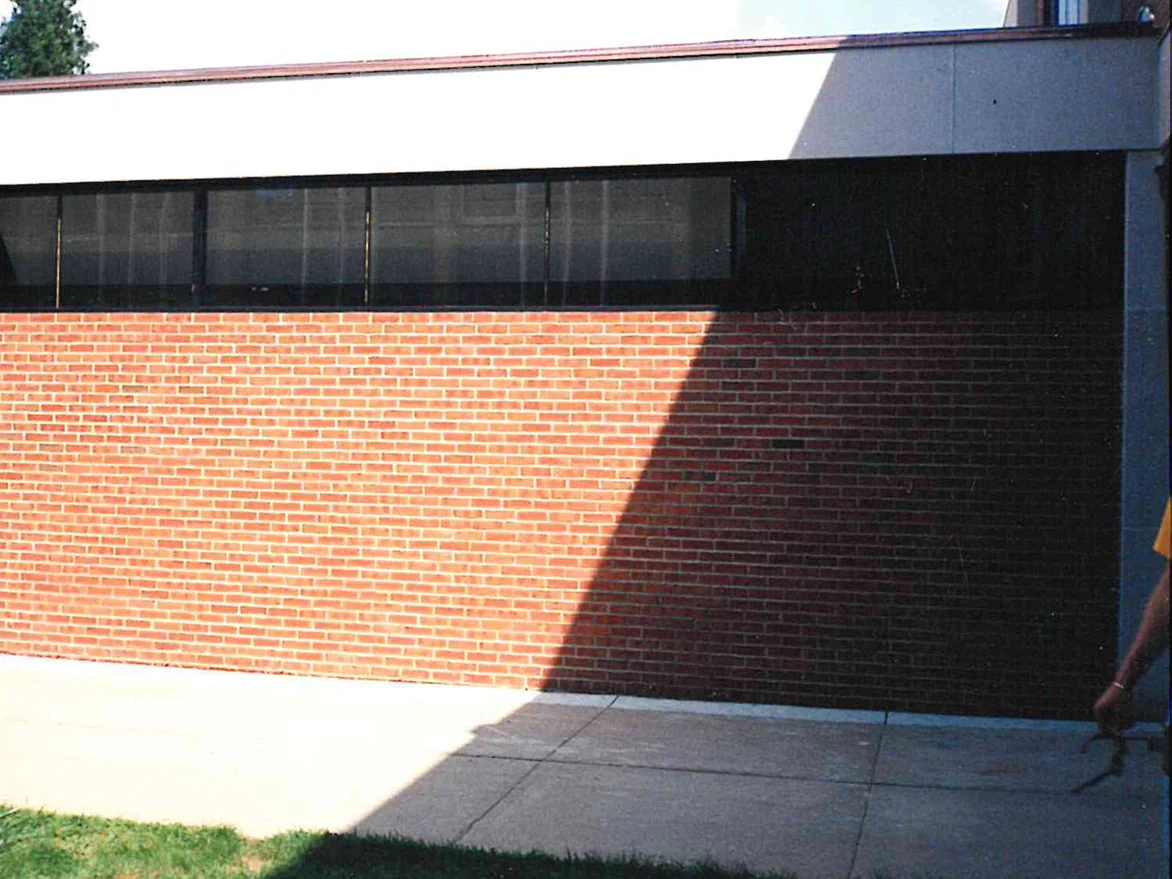 A single-story brick wall photographed straight on in 2007, the units reading as one even red range under a long band of dark clerestory glass