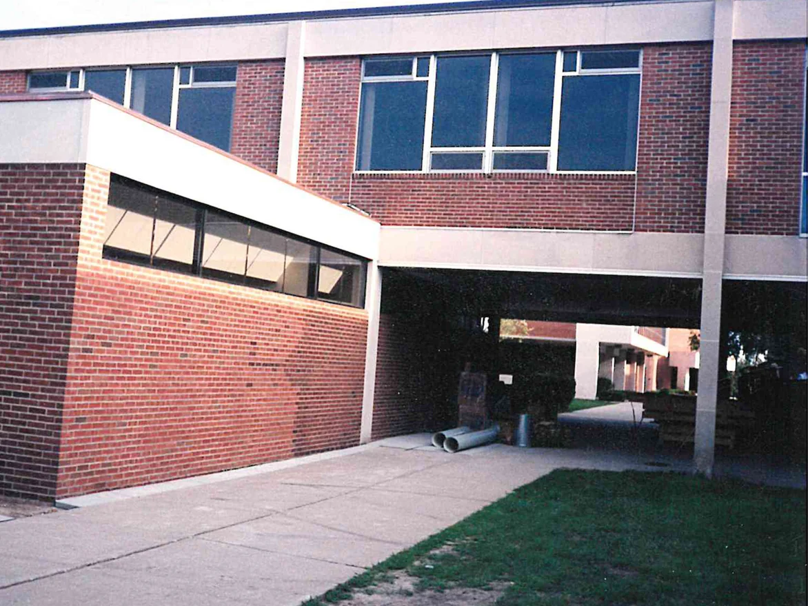 A single-story wing with sloping clerestory glazing in 2007, its red brick carrying darker mismatched areas, set against a two-story block and a covered breezeway