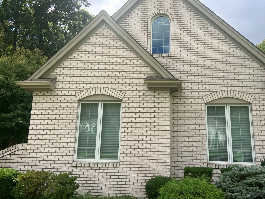 Two stacked gables of the house in 2019, an arched attic window above two windows with brick arches over them, the wall one even cream color