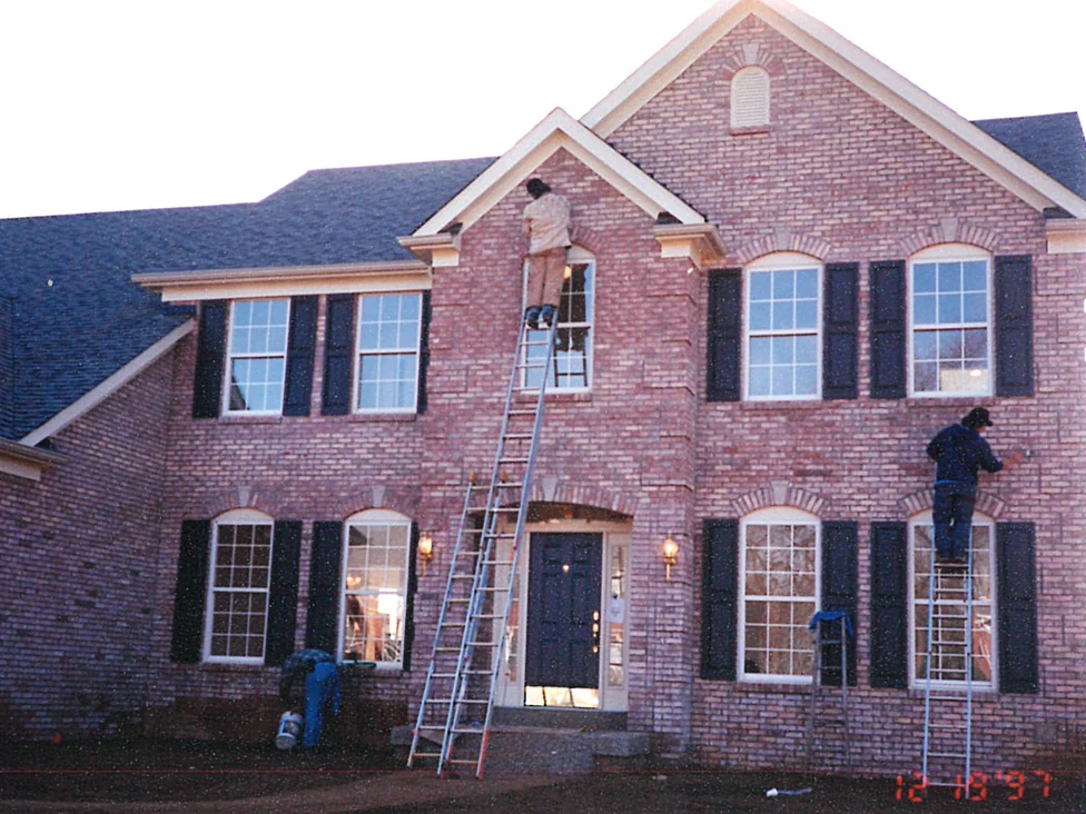 Two applicators on ladders working across the front of the house in 1997, the brick lighter and more even where they have already passed
