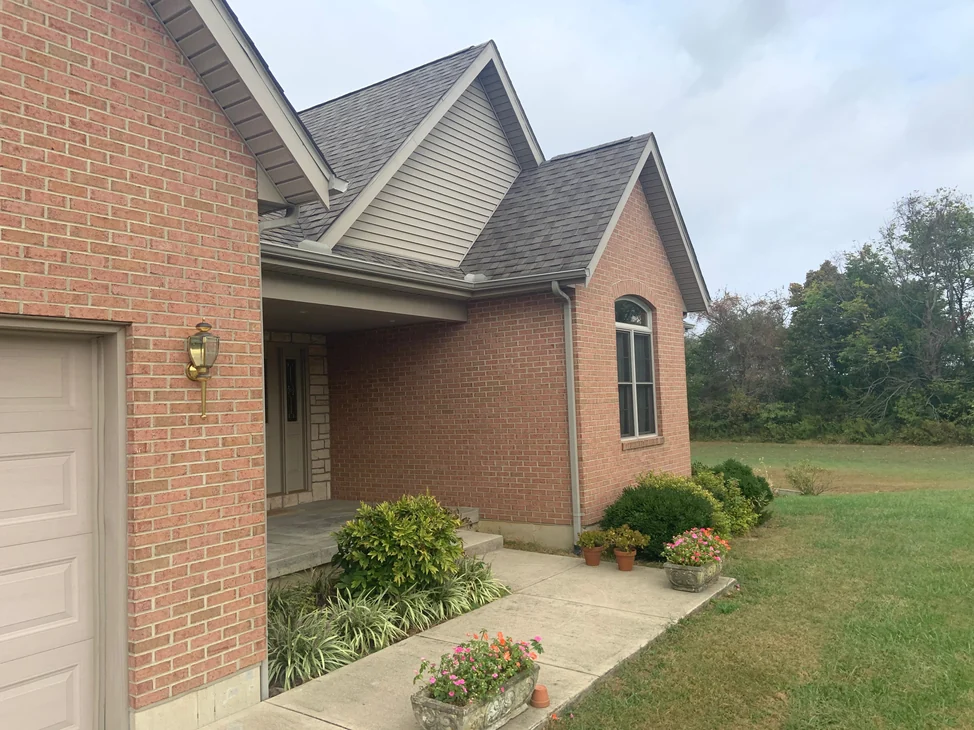 The front of the house in 2019, brick running from the garage gable past the covered entrance to a gabled wing with an arched window